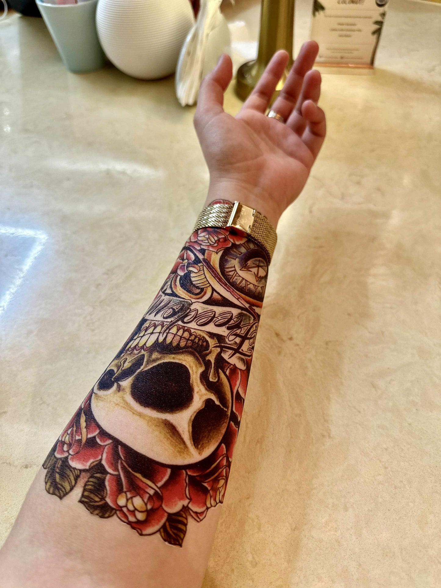 Arm with a detailed tattoo of a skull and floral design on a light-colored floor.