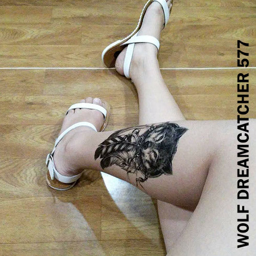 Legs of a woman sitting on the floor while showing her temporary tattoo sticker on the left with wolf dream catcher design.
