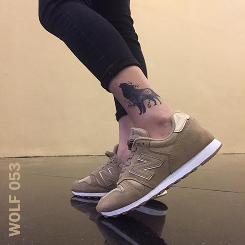 Woman's leg and foot wearing brown shoes and wolf moon temporary tattoo on her leg.