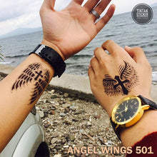 Load image into Gallery viewer, Two men, showing their hand with a temporary tattoo on the beach with winged cross design.