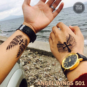 Two men, showing their hand with a temporary tattoo on the beach with winged cross design.