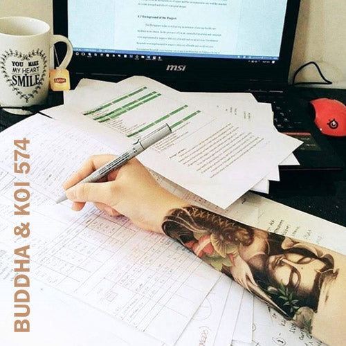 Woman's arm with Buddha and Koi Fish temporary tattoo sticker while writing her notes in front of a laptop.