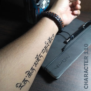 Man's arm with a Chinese character temporary tattoo on top of a wooden table with his notebook and pen.