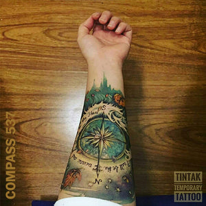 Woman's arm with compass temporaray tattoo design, on top of a wooden table.