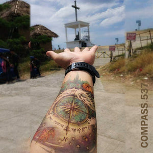 Man's arm with compass temporary tattoo design, with his hand pointing to a cross.
