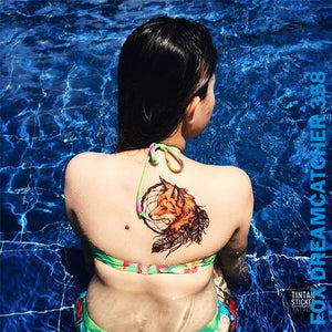 Woman's back on her temporary tattoo with fox dream catcher design while sitting on the swimming pool.