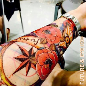 Man's arm with tintak temporary tattoo with compass, flowers, and the eye.
