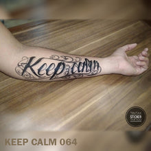Load image into Gallery viewer, Man&#39;s arm on top of a wooden table with &quot;Keep Calm&quot; temporary tattoo design.