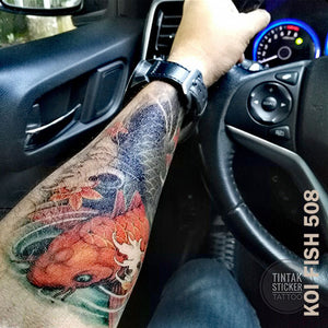Man's arm with colored koi fish temporary tattoo sticker while inside the car, holding the steering wheel.