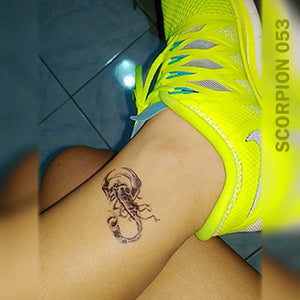 Woman's foot with scorpion temporary tattoo above her neon shoes.