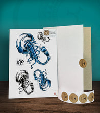 Load image into Gallery viewer, Tintak temporary tattoo sticker with black and blue scorpions design, with its hard board packaging.